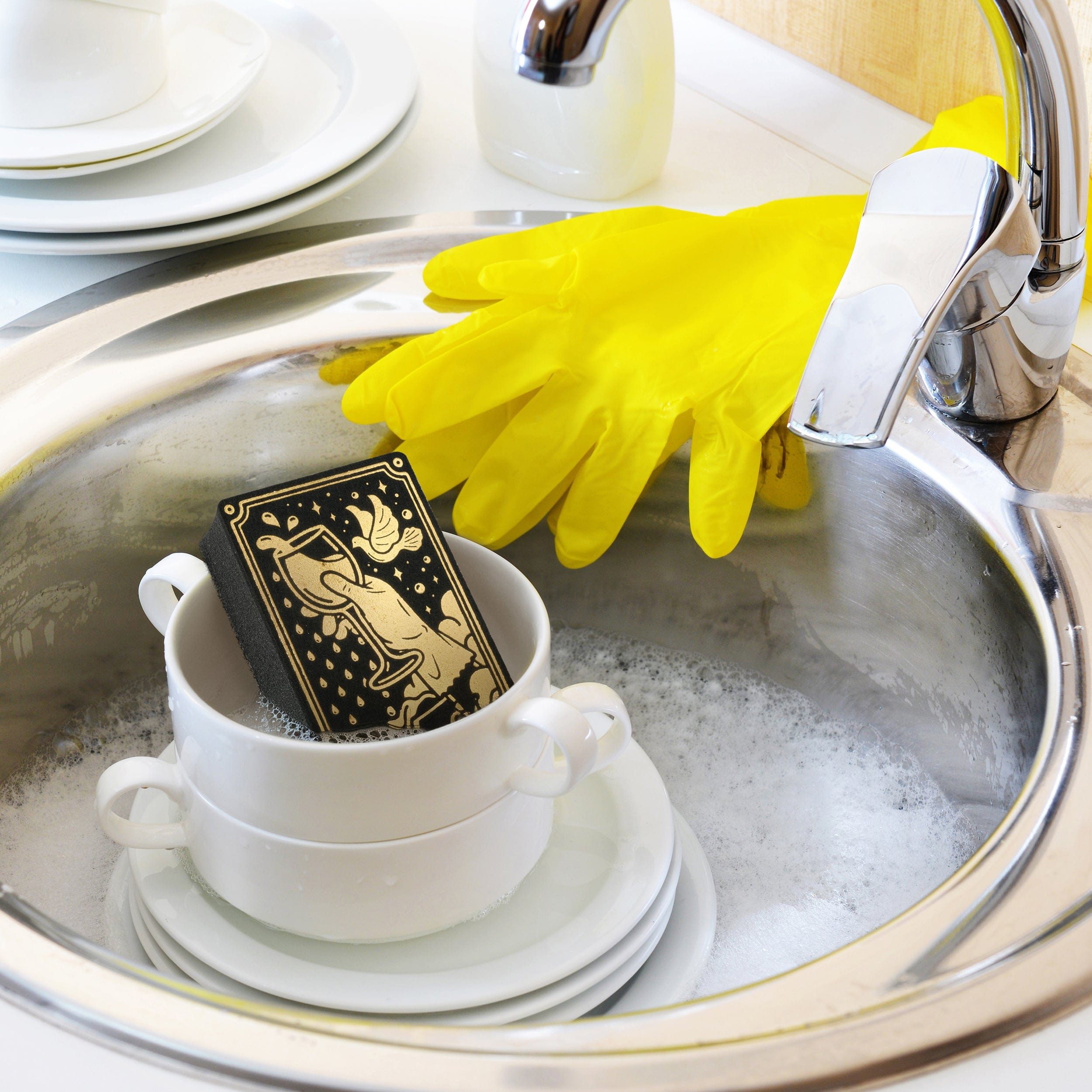 Dishwasher with dishes, a yellow glove, and a black tarot card sponge with gold design.