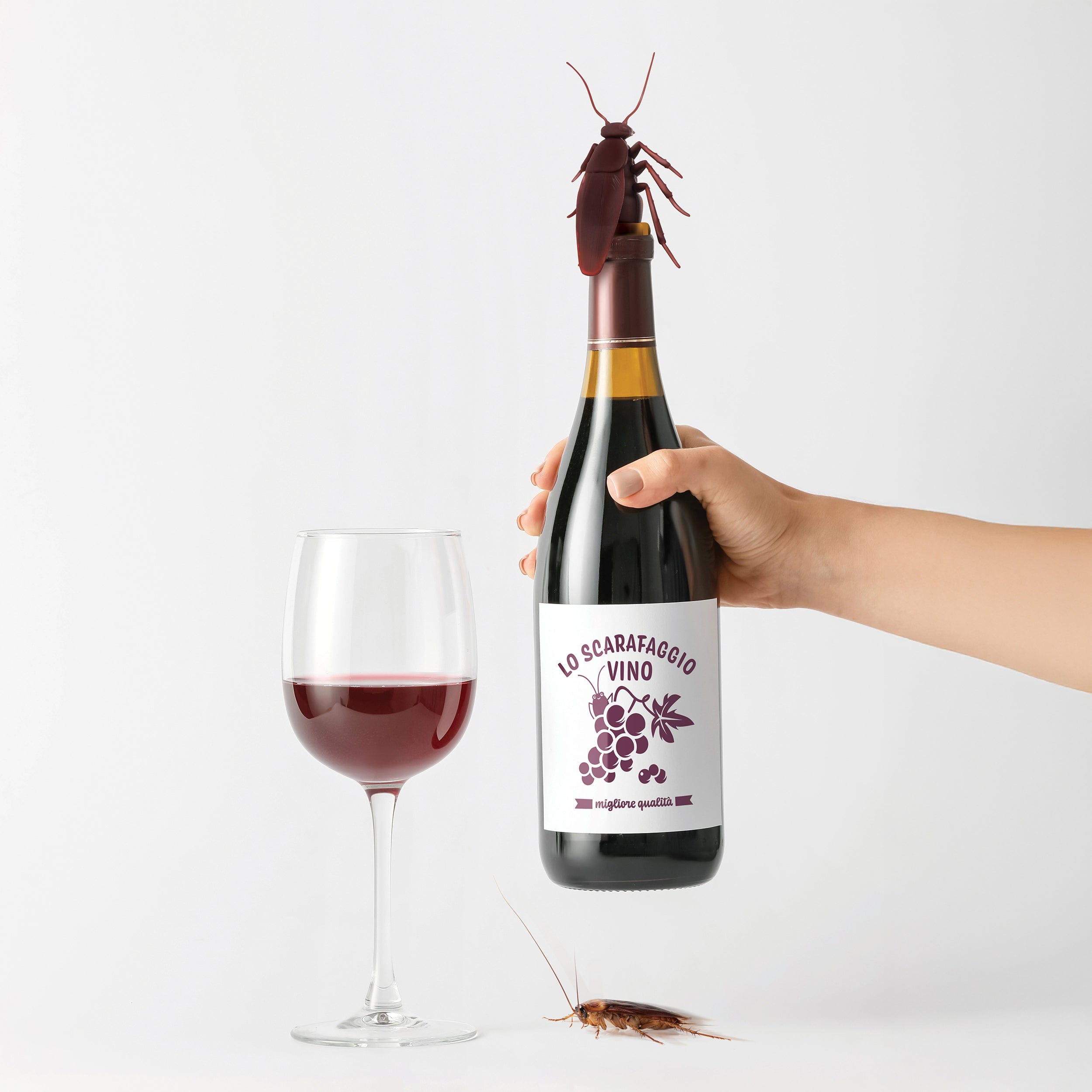 Bottle of 'Lo Scarafaggio Vino' wine with a hand holding it, a glass of wine, and a cockroach bottle stopper on a white background.