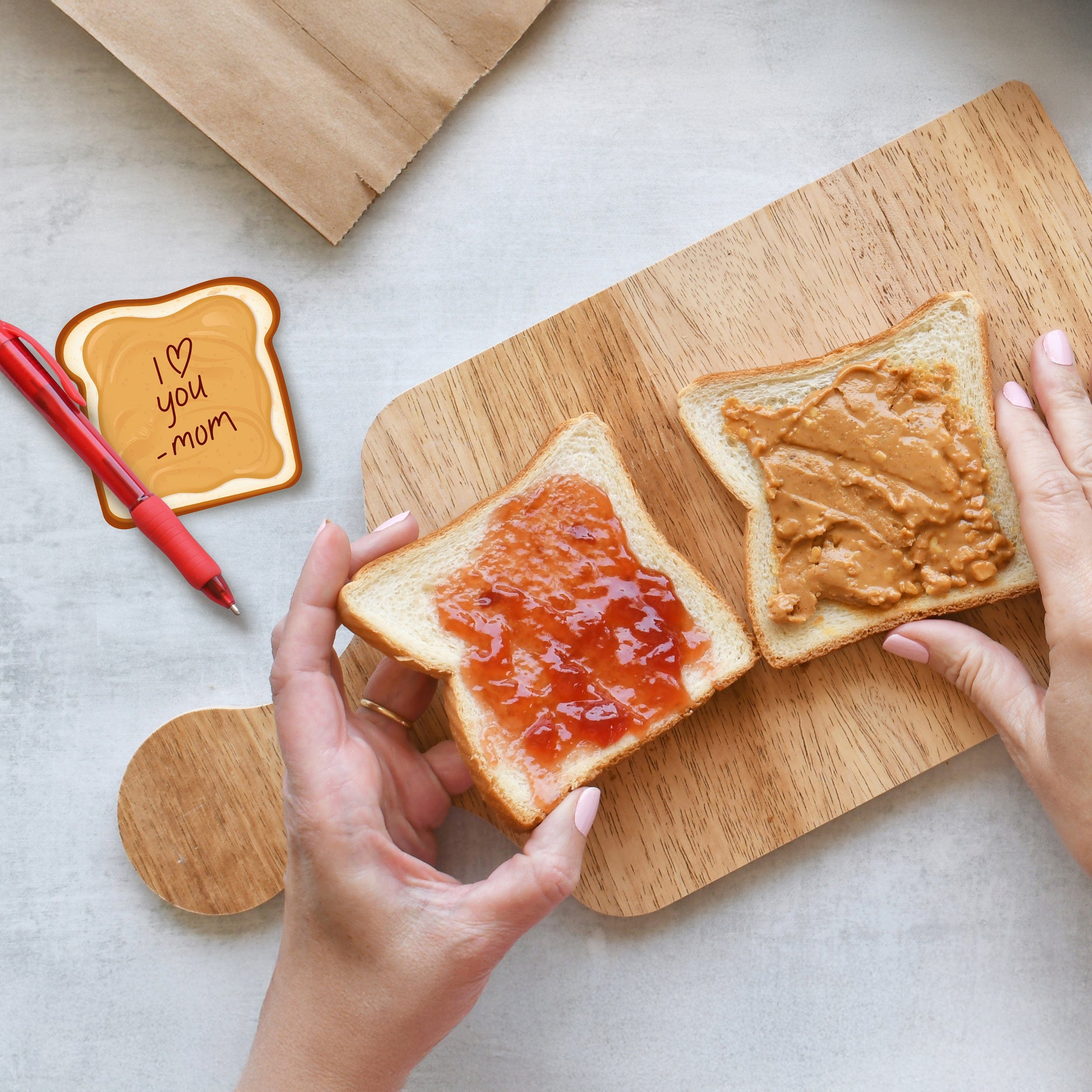 Two slices of toast with jelly and peanut butter on a wooden cutting board, with hands holding one slice.