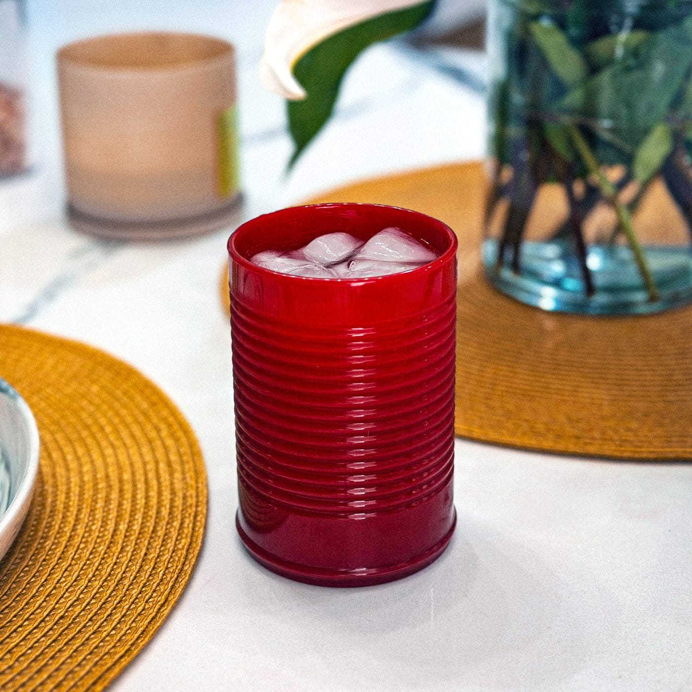 Red cranberry sauce silicone cup with ice on a table with a yellow placemat and a plant in the background