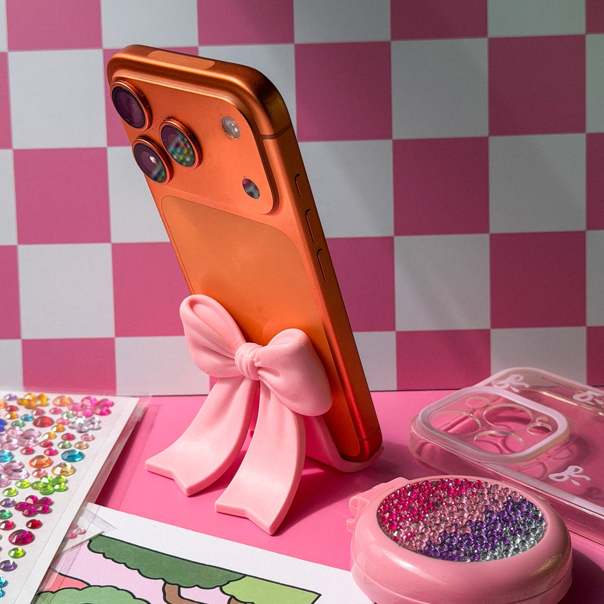 Angled view of an orange iPhone with triple cameras on a pink checkered background.