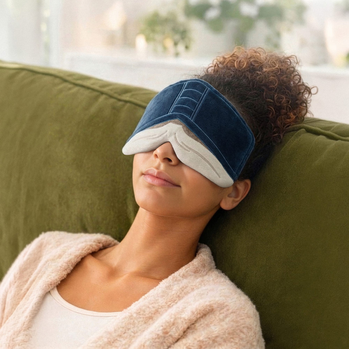 Person with curly hair wearing a blue sleep mask resting on a green couch