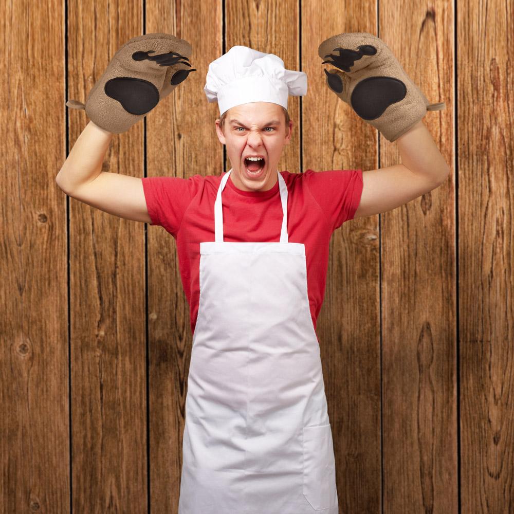 A chef making a growling expression and. wearing oven mitts that look like bear paws.