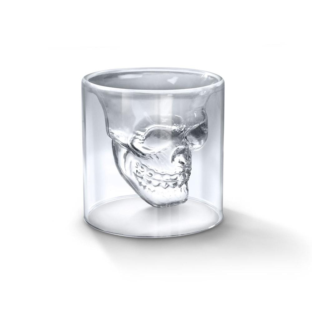 A clear crystal skull shot glass on a plain background.