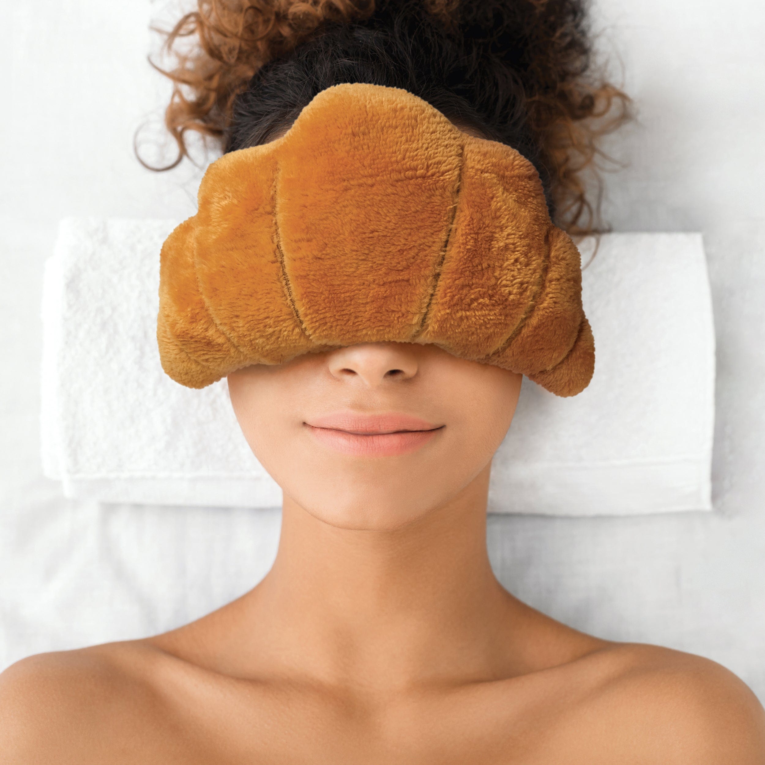Person relaxing and wearing a plush eye mask that looks like a croissant