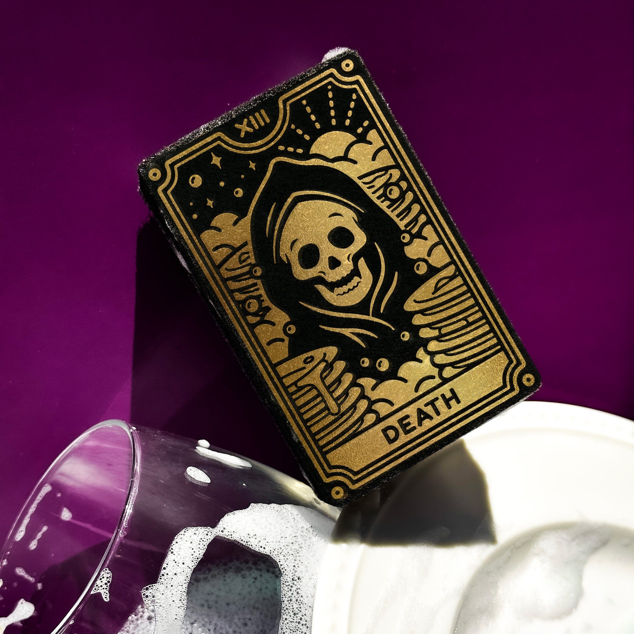tarot card sponge with a grim reaper design on a pile of dishes with a purple background