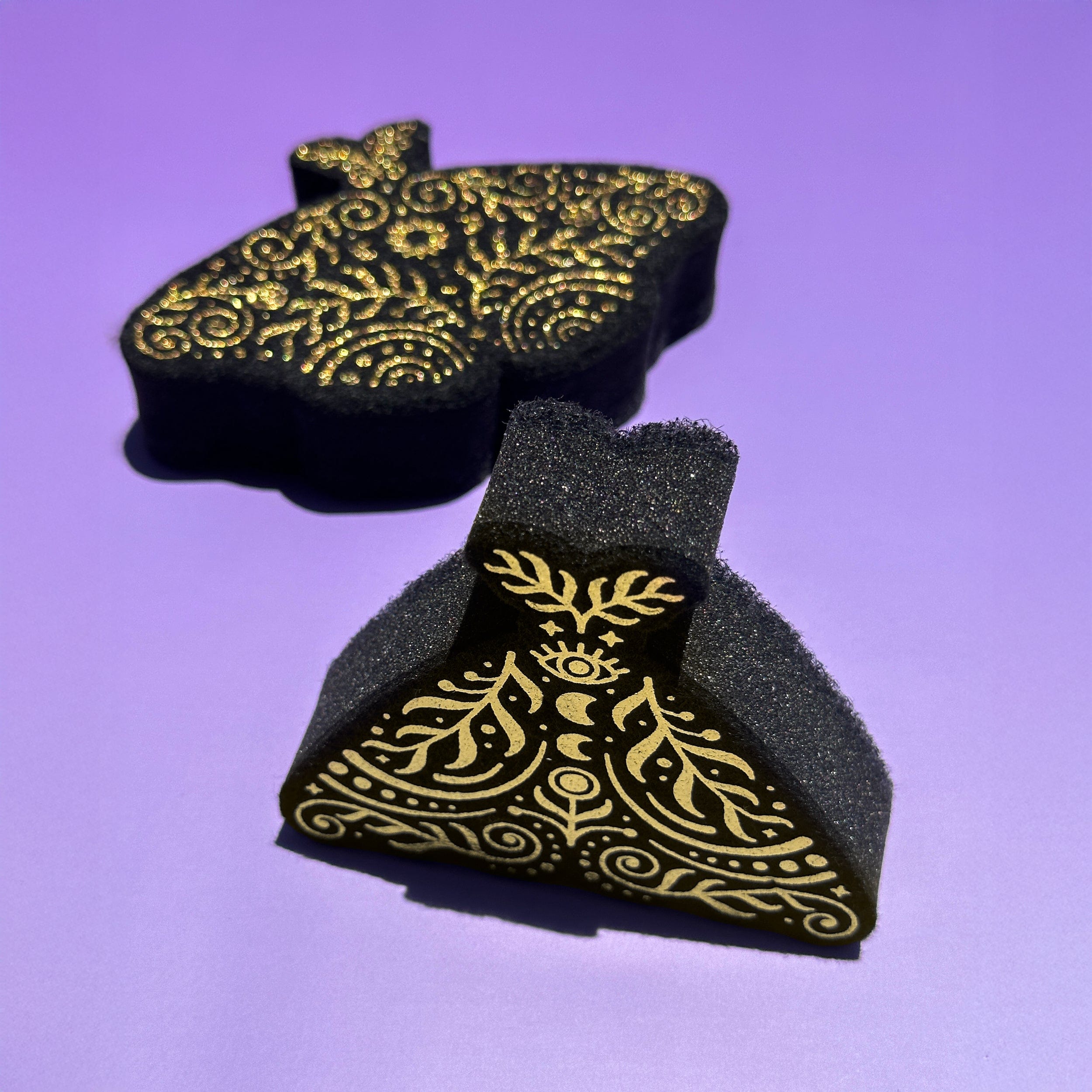 Black moth kitchen sponges with gold patterns on a purple background