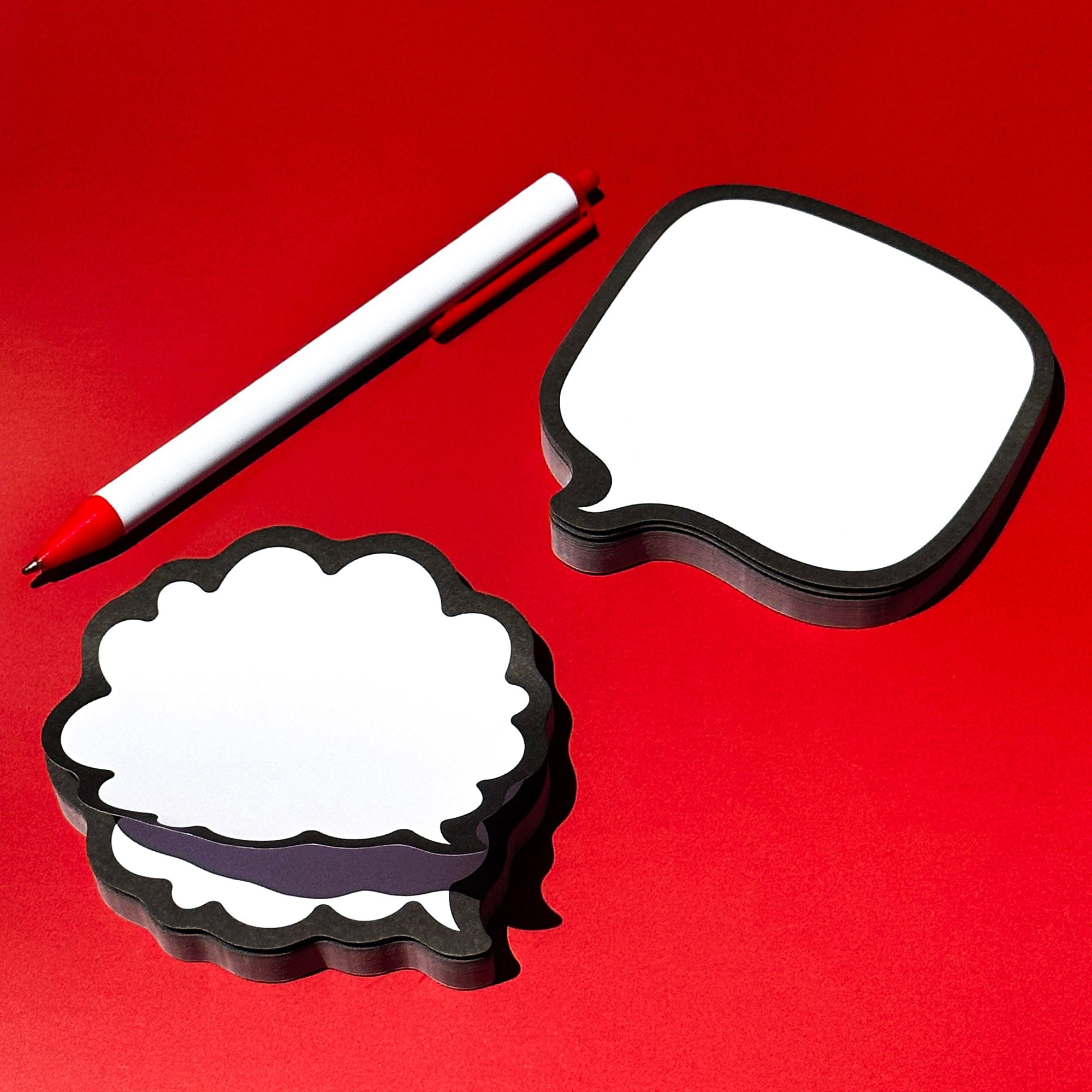 Two speech bubble-shaped notepads with a pen on a red background
