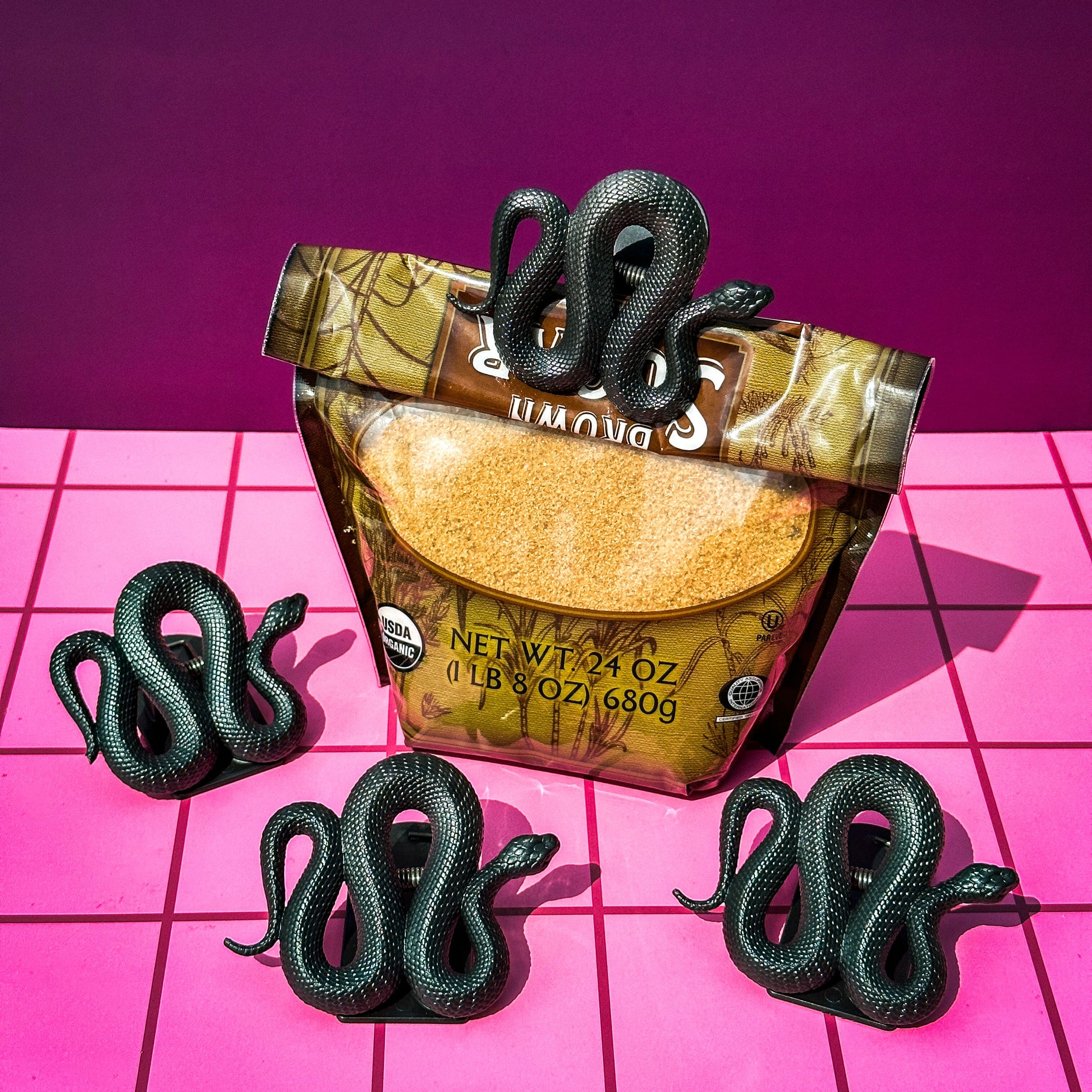 Packaged product with snake-shaped bag clips on a pink grid background