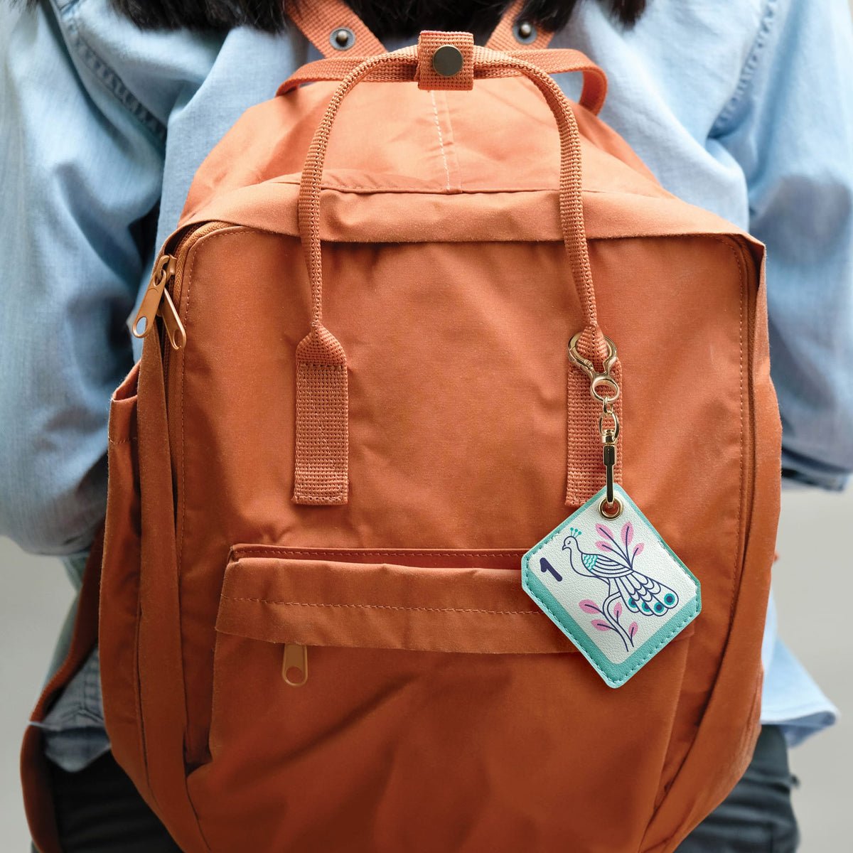 Mahjong tile bag charm attached to an orange backpack strap against blue denim. A trendy everyday accessory and unique holiday gift idea for game lovers.
