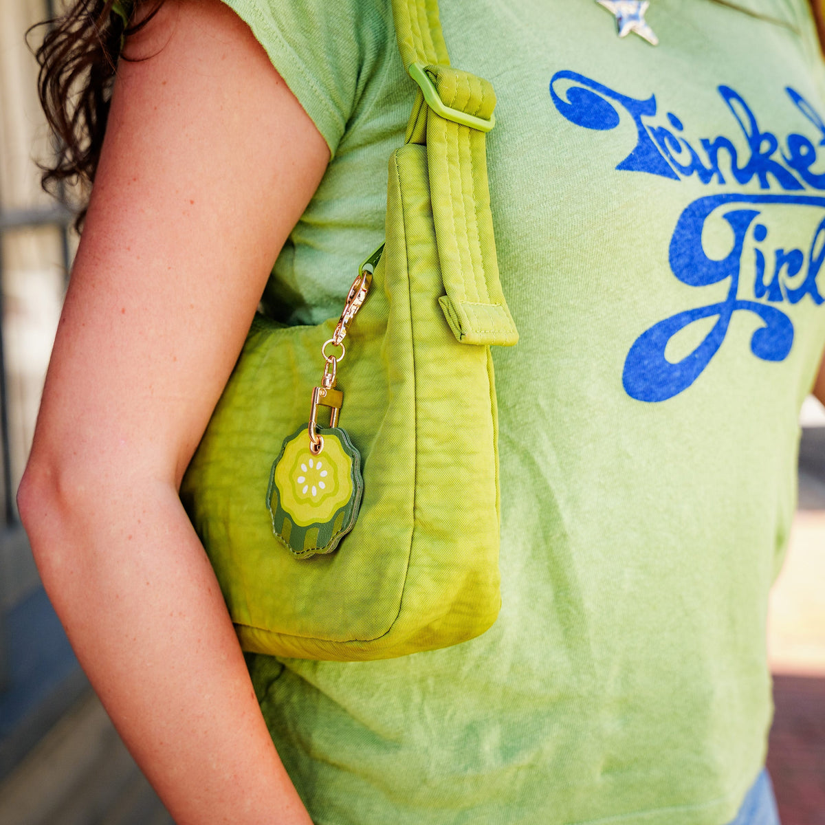 Pickle-shaped vegan leather bag charm attached to a fuzzy neon green handbag. A quirky holiday gift idea and unique stocking stuffer for teens and adults.