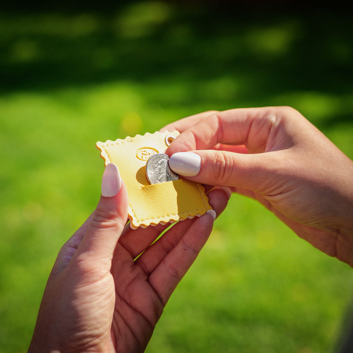 Person outdoors inserting a coin into the emergency quarter slot of the ravioli bag charm. A highly practical, top-rated holiday gift and useful stocking stuffer $10 and under.