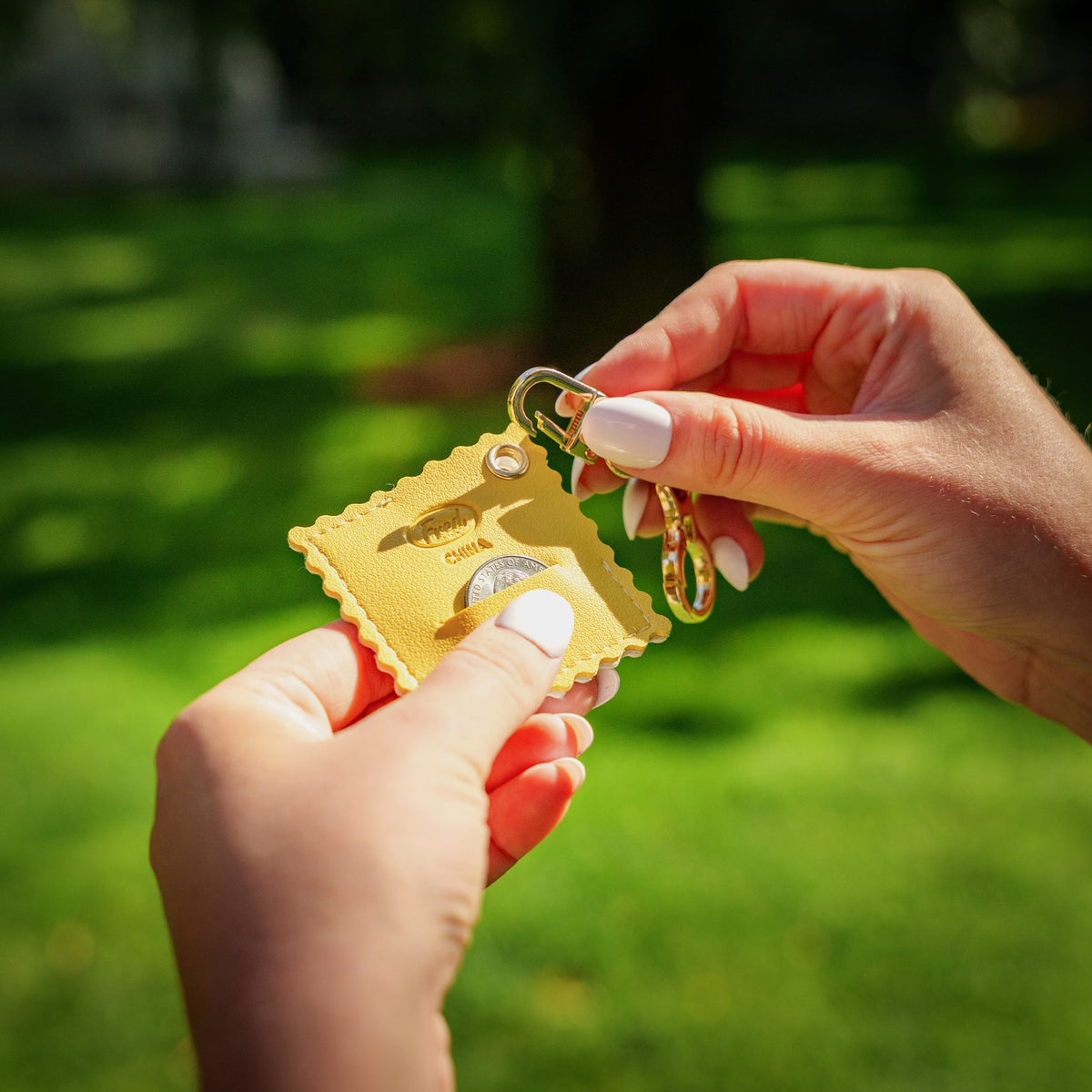 Hand holding the ravioli vegan leather bag charm outdoors, demonstrating the quarter slot in use. A functional, unique holiday gift for pasta lovers under $10.