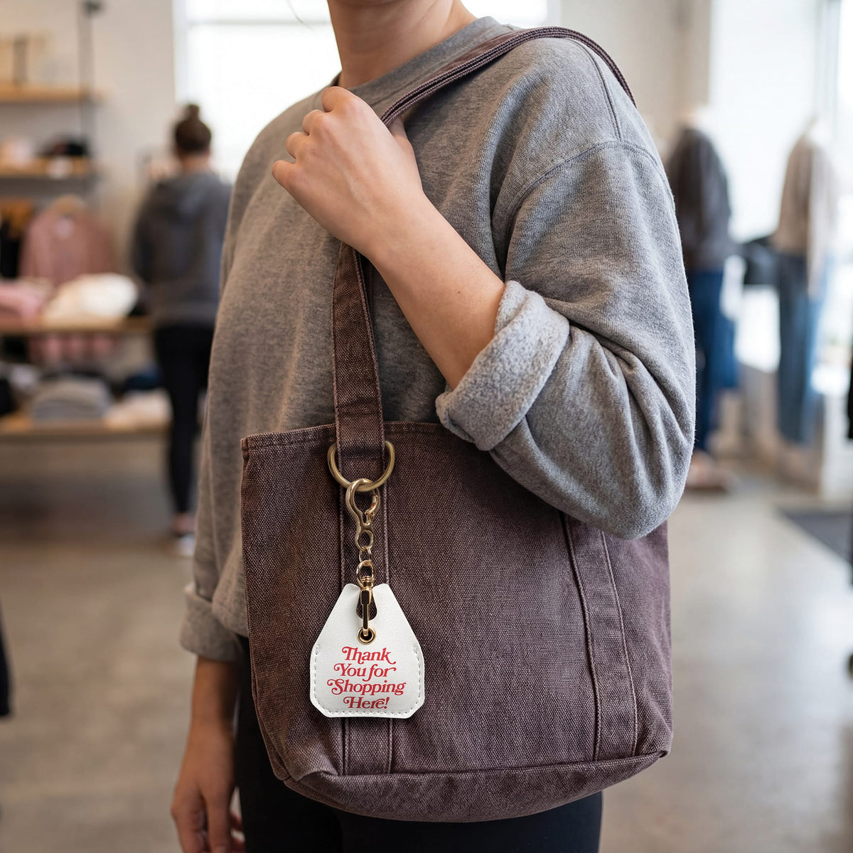 White 'Thank You for Shopping Here!' grocery bag charm clipped to a large brown canvas tote bag. A stylish, functional holiday gift idea and unique stocking stuffer for everyday errands.