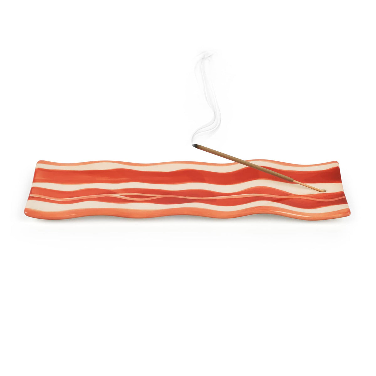 Incense stick burning on a wavy orange red striped ceramic plate with rising smoke