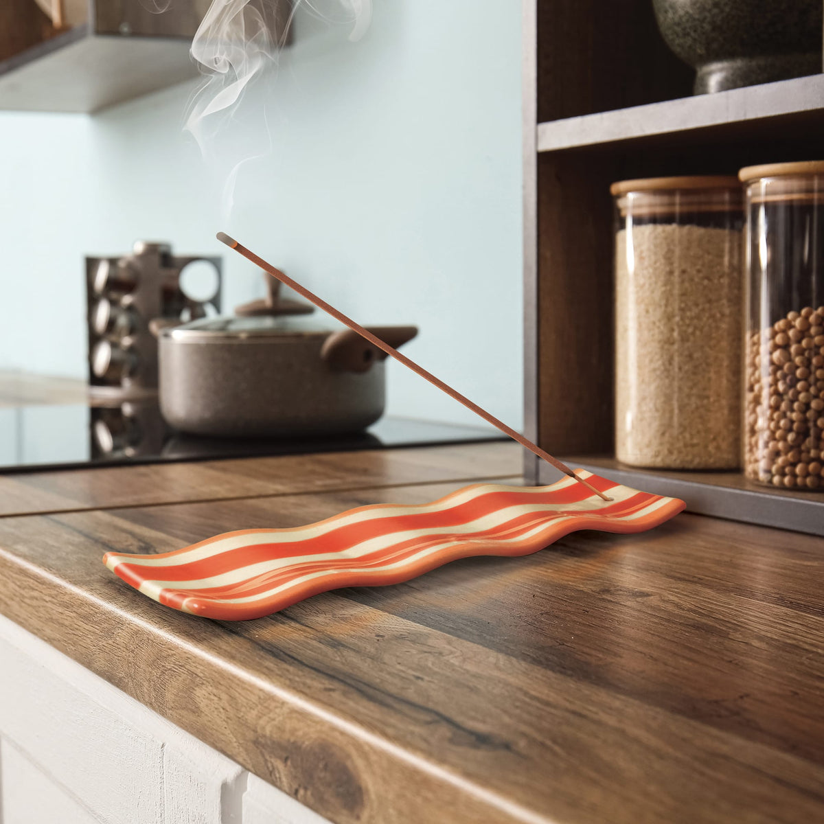 Incense burning in a kitchen scene with a pot on the stove and jars in the background, smoke curling upward