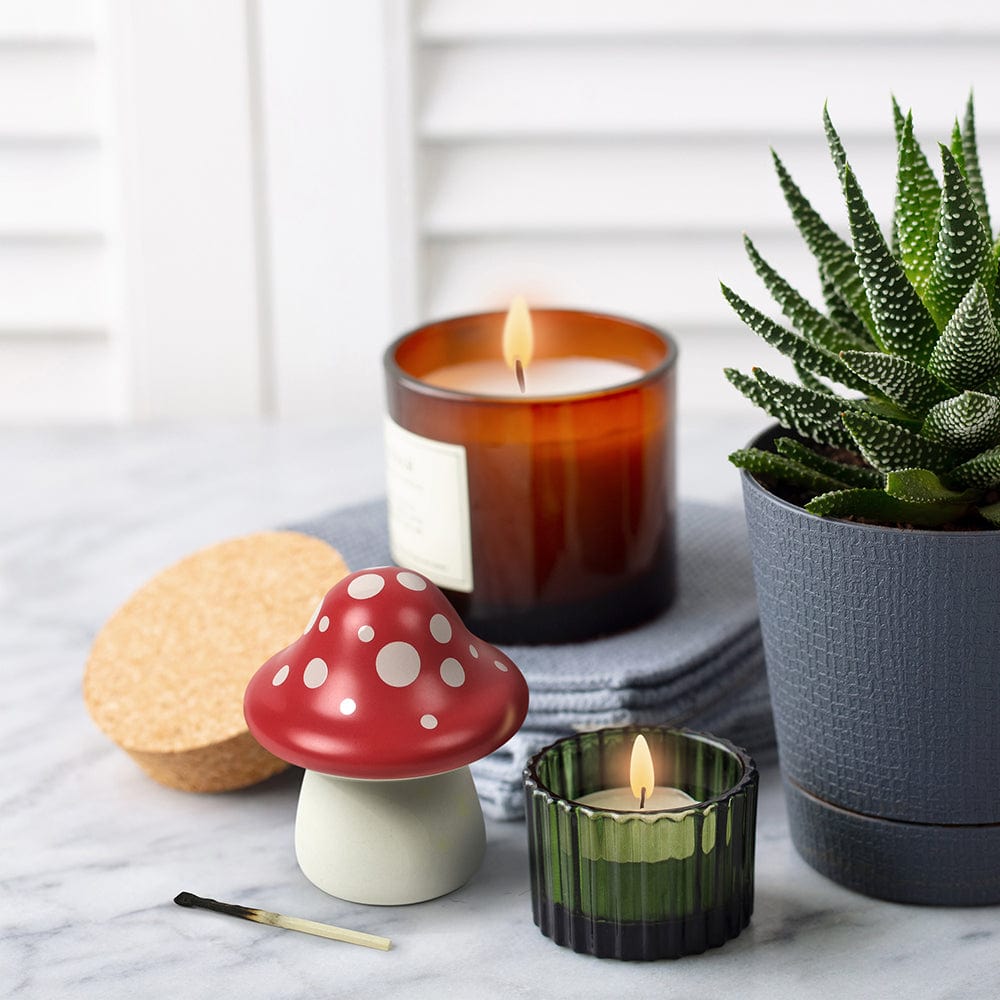 A ceramic mushroom on a marble countertop surrounded by lit candles and an aloe plant,